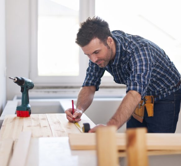 Smiling carpenter measuring wooden planks