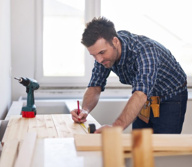 Smiling carpenter measuring wooden planks